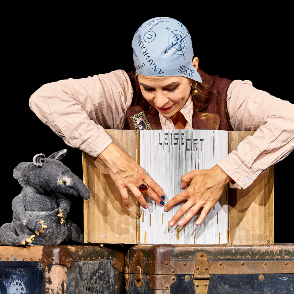 Szene aus dem Kindertheater „Pop-Up, Pirat!“: Piratin mit Überseekoffer und Tapir-Figur auf der Bühne