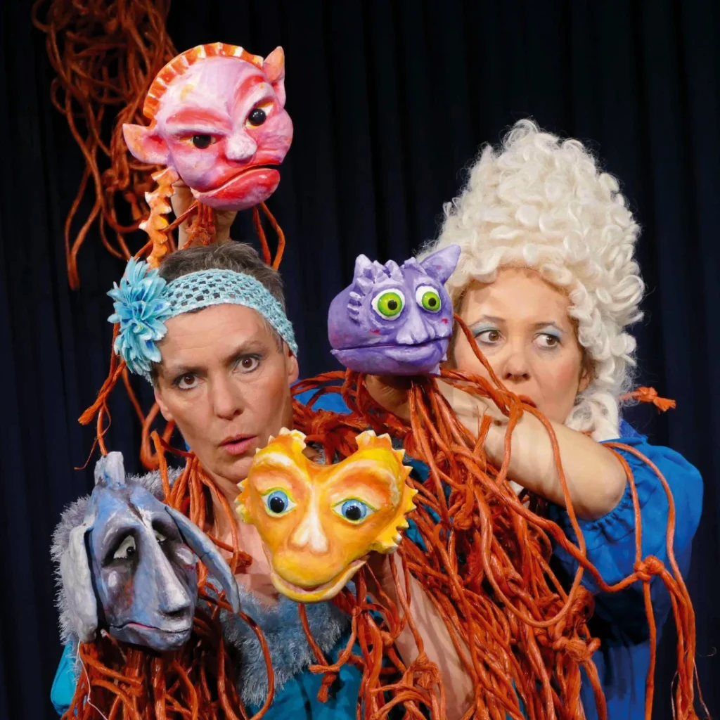Zwei Figurenspielerinnen mit bunten Puppenfiguren stellen verschiedene Gefühle dar – Szene aus dem Kindertheater „Knallwut“.